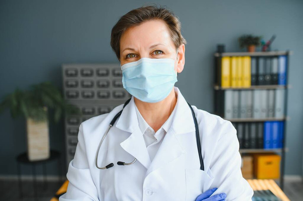 Portrait of a female doctor wearing face mask and holding her patient chart on digital tablet while standing at the hospital. - Fotoğraf, Görsel