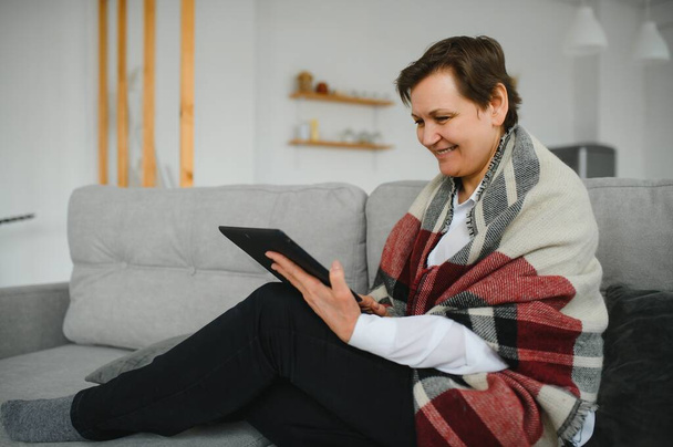 portrait of beautiful old woman using tablet pc and smiling, sitting on sofa at home - Photo, image