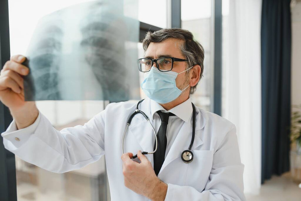 Médico usando máscara e olhando para radiografia de tórax - Foto, Imagem