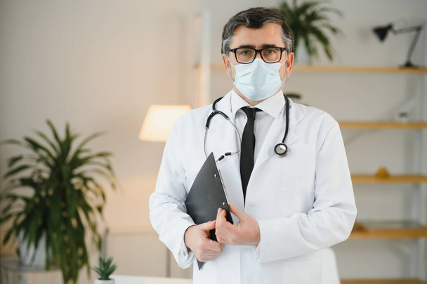 Portrait of healthcare worker. Image of senior male doctor wearing lab coat and standing at private clinic. - Zdjęcie, obraz