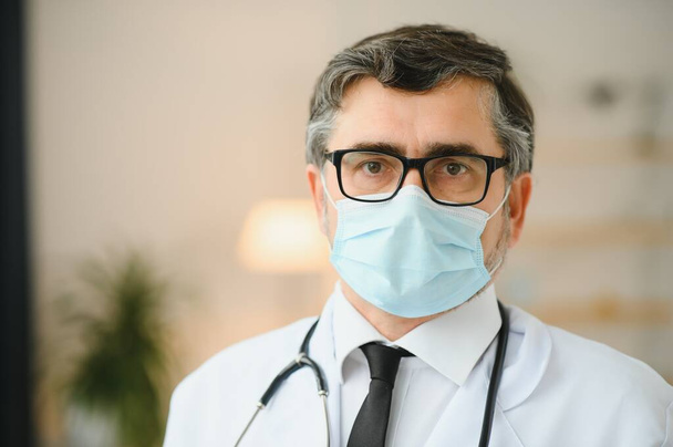 Mature old medical healthcare professional doctor wearing white coat, stethoscope, glasses and face mask. Medical staff health care protection concept. Portrait - Fotó, kép