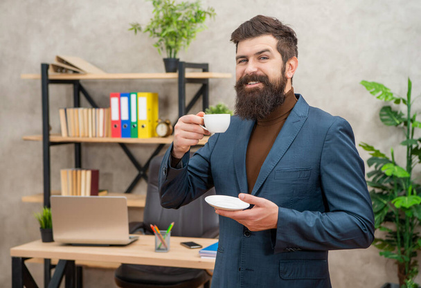 positive bearded business man drinking coffee in the office with copy space, morning - Φωτογραφία, εικόνα