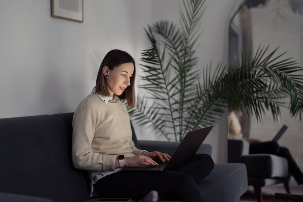 Жінка використовує ноутбук вдома у вітальні
 - Фото, зображення