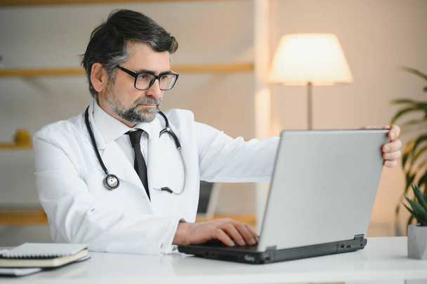Portrait of a serious doctor using laptop in medical office. - Foto, imagen