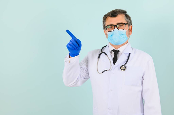 Male doctor, in a white coat and gloves, points to the side with his hands. next to the text space. blank on a blue background - Foto, imagen
