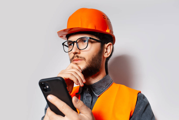 Studio portrét mladého stavebního dělníka na bílém, s chytrým telefonem v ruce. - Fotografie, Obrázek