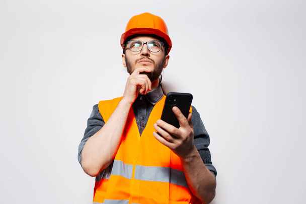 Studio portrait of young thoughtful construction worker using smartphone. - Photo, image