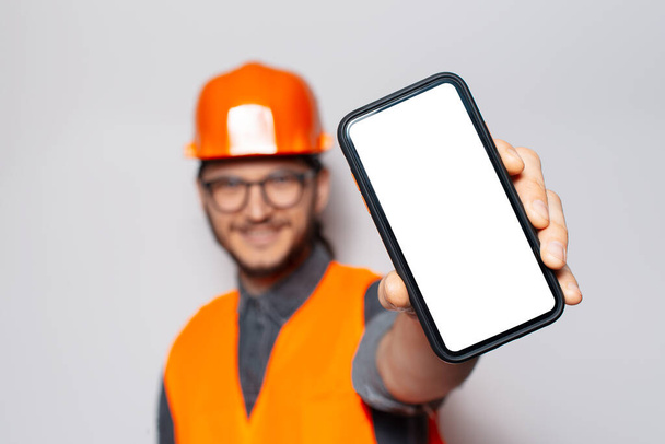 Trabajador de la construcción sosteniendo teléfono inteligente con pantalla en blanco sobre fondo blanco. - Foto, imagen