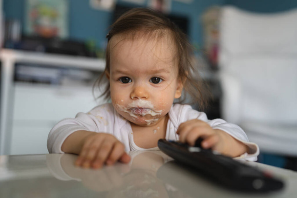 Un bebé pequeño niño caucásico desagradable niña con comida alrededor de su boca y en la cara sucia haciendo lío en la infancia en casa y creciendo espacio de copia de concepto - Foto, imagen