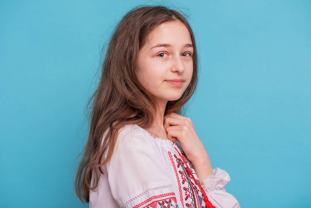 Portret van een 11-jarig meisje in Oekraïense geborduurde kleren. Meisje op een blauwe achtergrond. - Foto, afbeelding