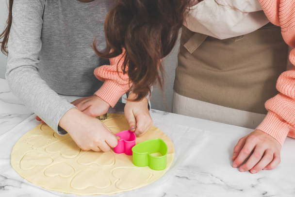 Two caucasian girls cut out shortbread dough with metal and plastic heart shapes. - Photo, Image