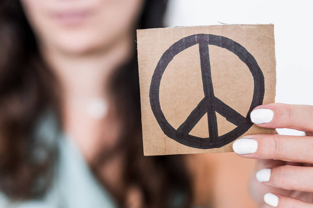 woman holding peace sign on a piece of cardboard pointing it towards the camera shot at shallow depth of field, concept of world peace and ending wars - Fotografie, Obrázek