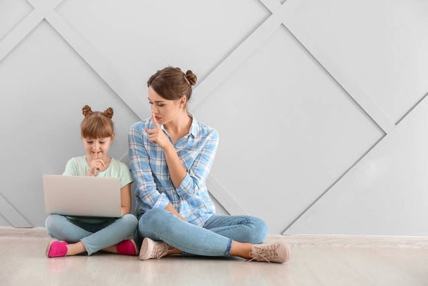 Portrait of mother and daughter with laptop showing silence gesture indoors - Photo, Image