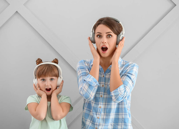 Portret van verbaasde moeder en dochter luisteren naar muziek op grijze achtergrond - Foto, afbeelding