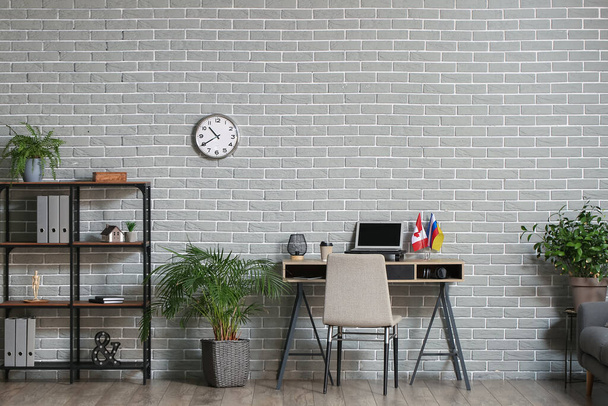 Workplace with laptop and different flags near light brick wall - Fotoğraf, Görsel