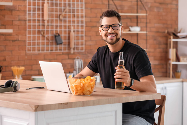 Hombre guapo con portátil bebiendo cerveza en la cocina - Foto, imagen
