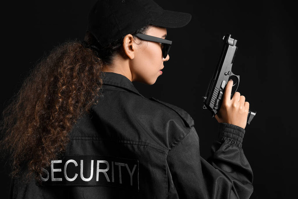 African-American female security guard with sunglasses and gun on dark background - Foto, afbeelding