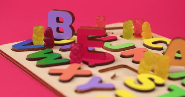 Holztafel mit Buchstaben und leckeren Gummibärchen auf rotem Hintergrund, Nahaufnahme - Filmmaterial, Video
