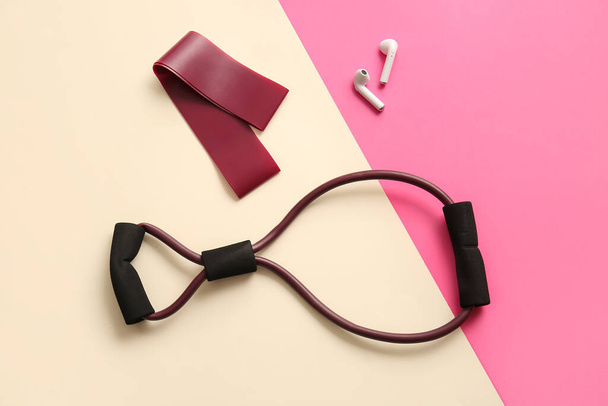 Fitness expander, elastische band en oortelefoon op kleur achtergrond - Foto, afbeelding