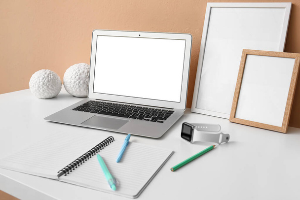 laptop moderno, smartwatch e suprimentos de papelaria na mesa perto da parede de cor - Foto, Imagem