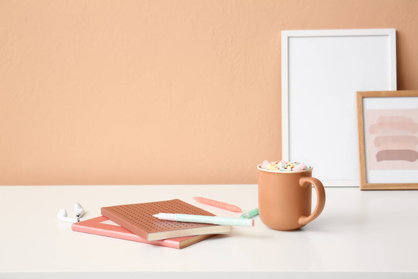 Stationery supplies, earphones and cup with cacao on table near color wall - Photo, Image