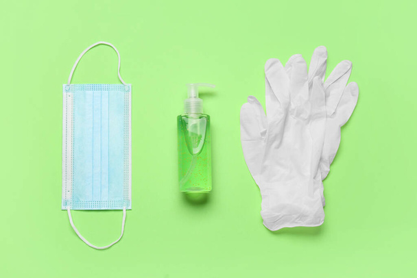 Medical mask, gloves and bottle of antiseptic on green background - Photo, Image