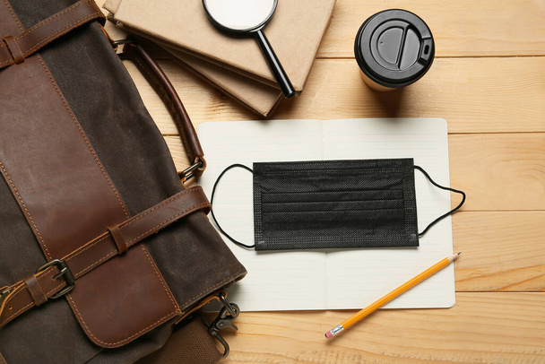 Bag, notebooks, magnifier, paper cup of coffee and medical mask on wooden background - Φωτογραφία, εικόνα