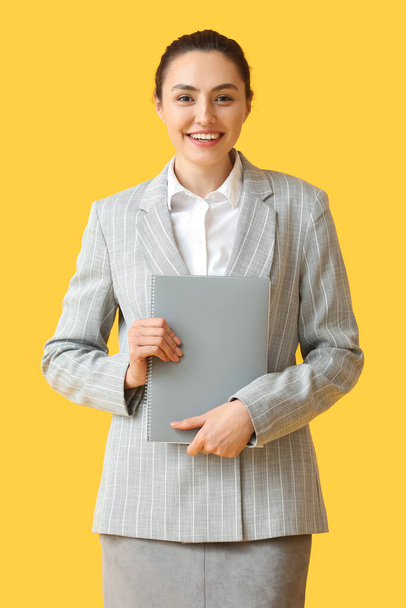 Jolie jeune femme d'affaires avec dossier sur fond jaune - Photo, image