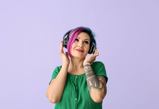 Beautiful woman with unusual hair and tattoo listening to music on color background - Foto, afbeelding