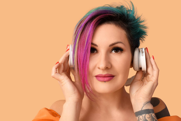 Beautiful woman with unusual hair listening to music on orange background - Photo, image