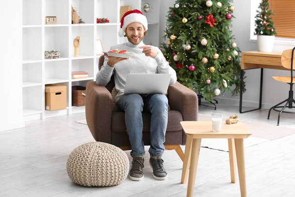 Noel Baba şapkalı genç adam evde Noel kurabiyeleriyle sohbet ediyor. - Fotoğraf, Görsel