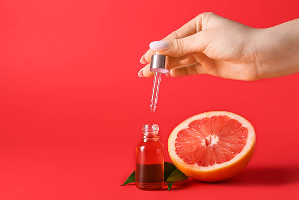 Weibliche Hand mit einer Flasche ätherischem Grapefruitöl auf rotem Hintergrund, Nahaufnahme - Foto, Bild