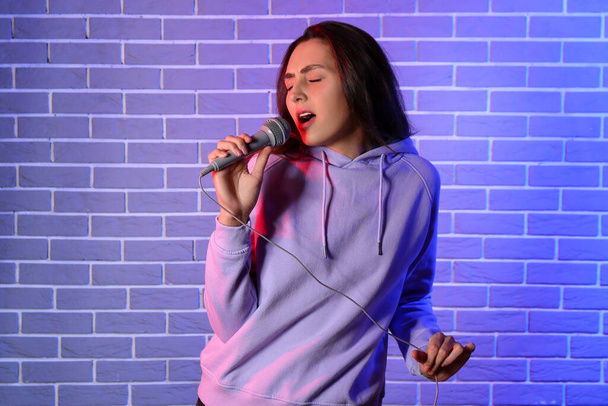Cool fiatal nő énekel színes tégla háttér - Fotó, kép