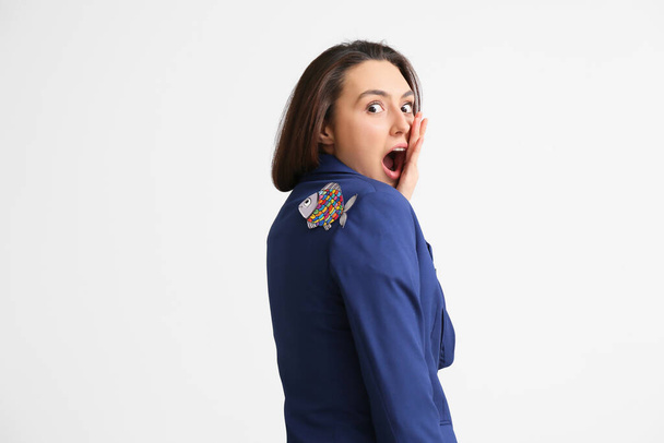 Shocked young woman with paper fish attached to her back on grey background. April fools day celebration - Foto, imagen