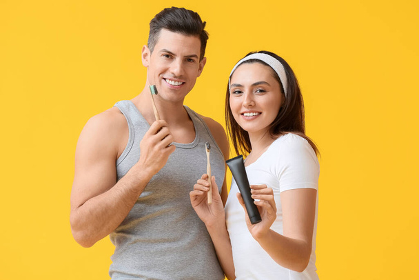 Mladý pár s aktivním uhlím zubní pasta a štětce na žlutém pozadí - Fotografie, Obrázek