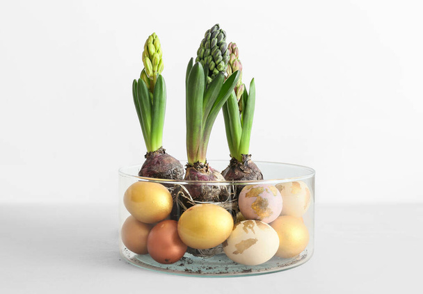 Стеклянный горшок с красивыми гиацинтовыми растениями и пасхальными яйцами на светлом фоне - Фото, изображение