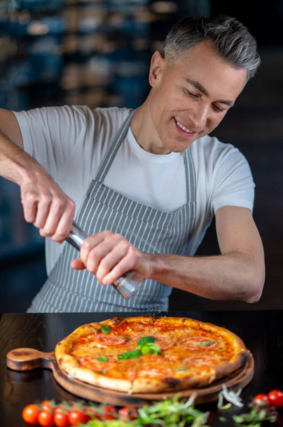 Un hombre en delantal haciendo pizza vegetariana con tomates cherry - Foto, imagen