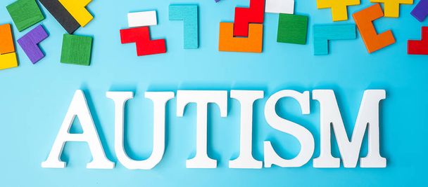 AUTISM text with colorful wood puzzle pieces, geometric shape block on blue background. Concepts of health, Autistic Spectrum disorder and world Autism awareness day - Photo, Image