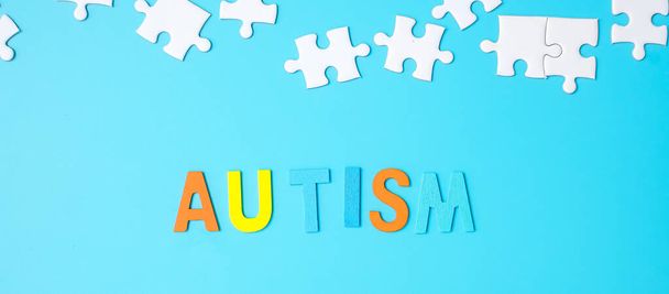 青い背景に白いパズルジグソーパズルの作品と自閉症テキスト。健康、自閉症スペクトラム障害、世界の概念｜自閉症の意識の日 - 写真・画像