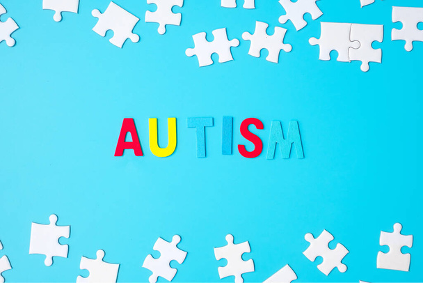 AUTISM szöveg fehér puzzle kirakós darabok kék háttérrel. Az egészség fogalma, az autista spektrumzavar és az autizmus világnapja - Fotó, kép