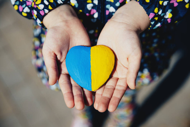 Pequeño niño sostiene piedra en forma de corazón con bandera nacional de Ucrania o himno - Foto, imagen