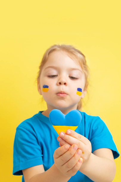 Το κορίτσι κατέχει μια καρδιά του κίτρινου και μπλε χρώματος της ουκρανικής σημαίας. - Φωτογραφία, εικόνα
