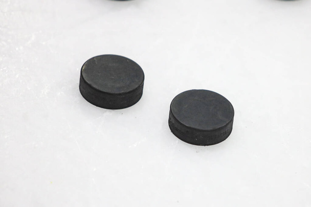 Two black pucks laying on ice hockey rink. Photo taken inside ice hockey rink before training. - Photo, Image