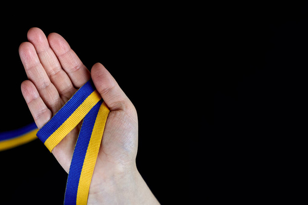 Ribbon in the color of the Ukrainian flag in the hand of a woman on a black background, copy space. - Foto, Bild