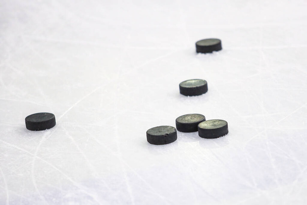 Multiple black Ice Hockey pucks laying on Ice rink ground. Photo taken inside arena, during training. - Photo, Image