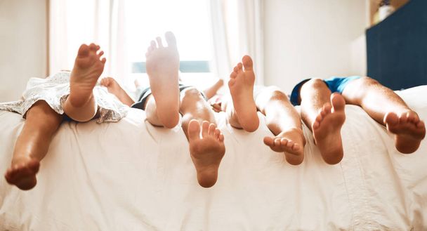 Felteszik a lábukat egy mókás nap után. Közelkép gyerekekről, akik mezítláb fekszenek otthon az ágyon.. - Fotó, kép