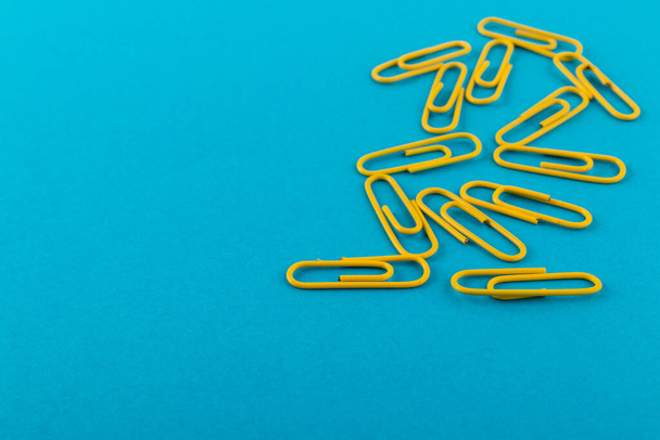 Colored paper clips. Yellow paper clips macro close up isolated on a blue background with copy space. - Foto, afbeelding