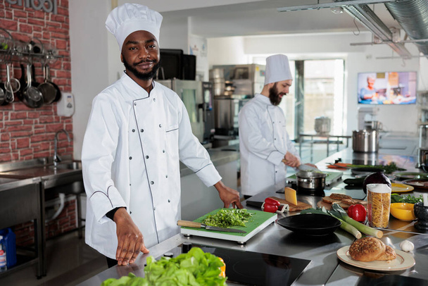 Кваліфікований шеф-кухар в уніформі для приготування їжі під час приготування інгредієнтів для страви на професійній кухні ресторану
. - Фото, зображення