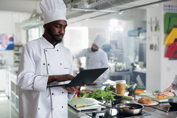 Gourmetküche Chefkoch mit Laptop auf der Suche nach gastronomischen Rezepten und Garnierungsideen in der Restaurantküche. - Foto, Bild