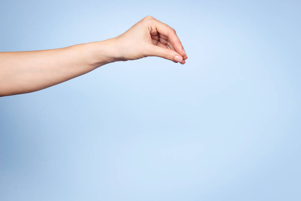 Handbewegung der Frau. Die weibliche Hand hält oder pflückt etwas Isoliertes auf hellblauem Hintergrund. Frontansicht - Foto, Bild
